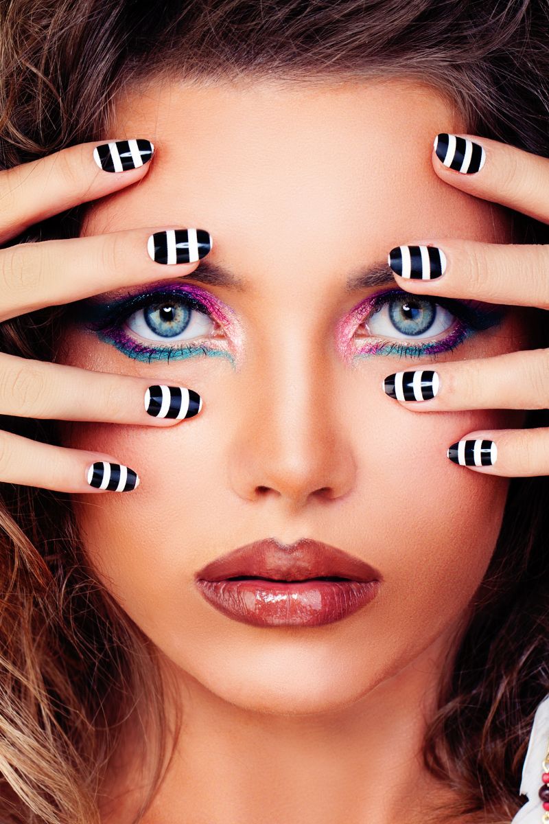 Close-up of a woman with colorful eye makeup and striped nail wraps.