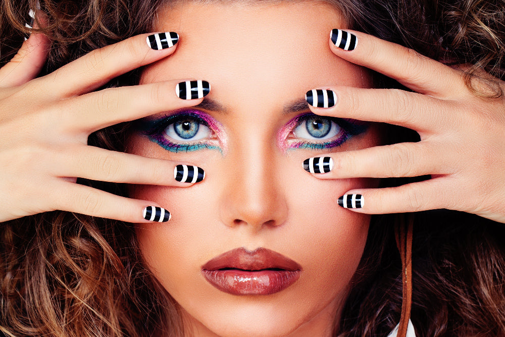 Woman with colorful eye makeup and striped nail wraps covering her eyes.